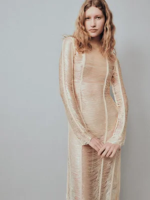 A model poses in a textured cream fringe long-sleeve dress against a neutral grey studio backdrop.