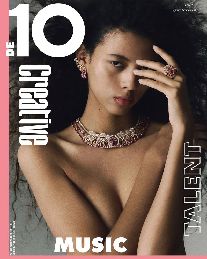 Close-up portrait of a woman wearing a jeweled necklace and rings against a grey background with magazine typography.