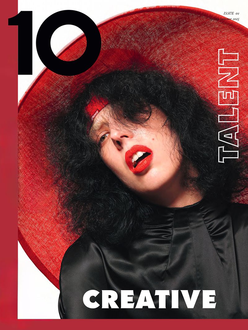 Magazine cover featuring a person with dark hair and red lipstick wearing a large red hat and black satin top, with text overlay.