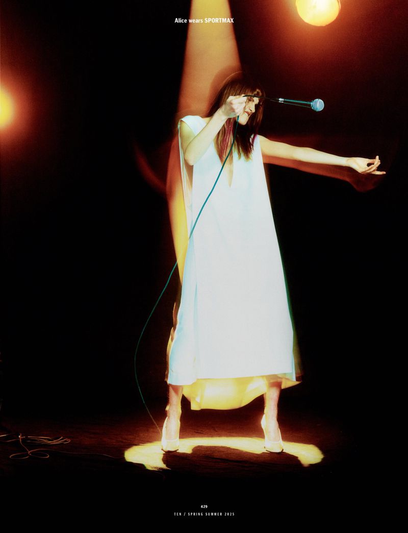 Woman in white dress holding a microphone under dramatic spotlight for 10 Magazine editorial