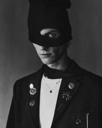 Portrait of a male model wearing a black balaclava beanie and dark jacket adorned with pins for Zara