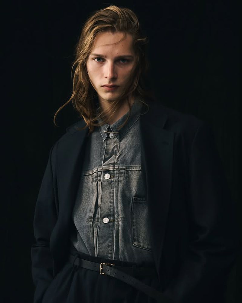 Model Cosme Voisin wearing an oversized black blazer over a grey denim jacket against a black backdrop.