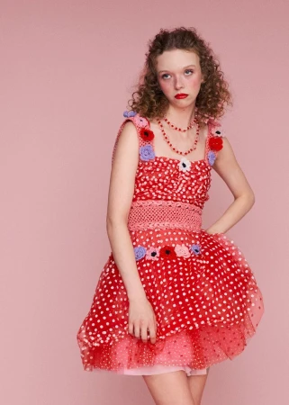 Model Lily Nova wears a red polka-dot tulle mini dress adorned with crochet flowers against a solid pink backdrop for Ryan LO.
