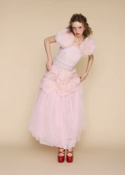 Model Lily Nova in a pink tulle dress with puff sleeves and red platform shoes standing against a beige backdrop.