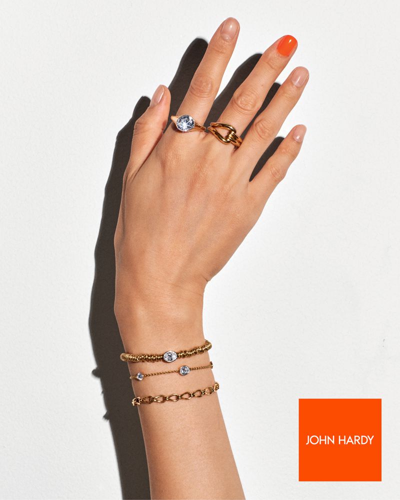 Hand with gold rings and bracelets. Woman's hand features fine jewelry in gold with gemstones. One fingernail is painted orange.