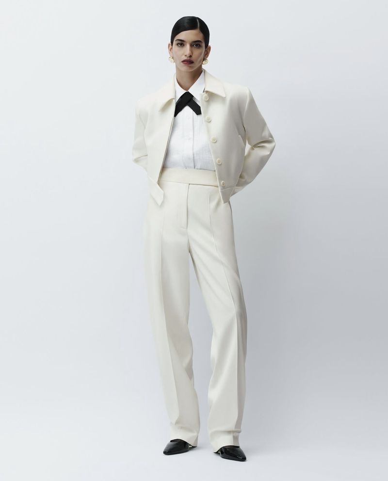 Portrait of an adult female model in an off-white suit with a black bow tie in a studio, showcasing fashion and style.