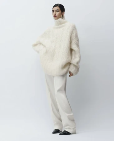 Model wearing a fluffy white turtleneck sweater and light trousers against a neutral background.