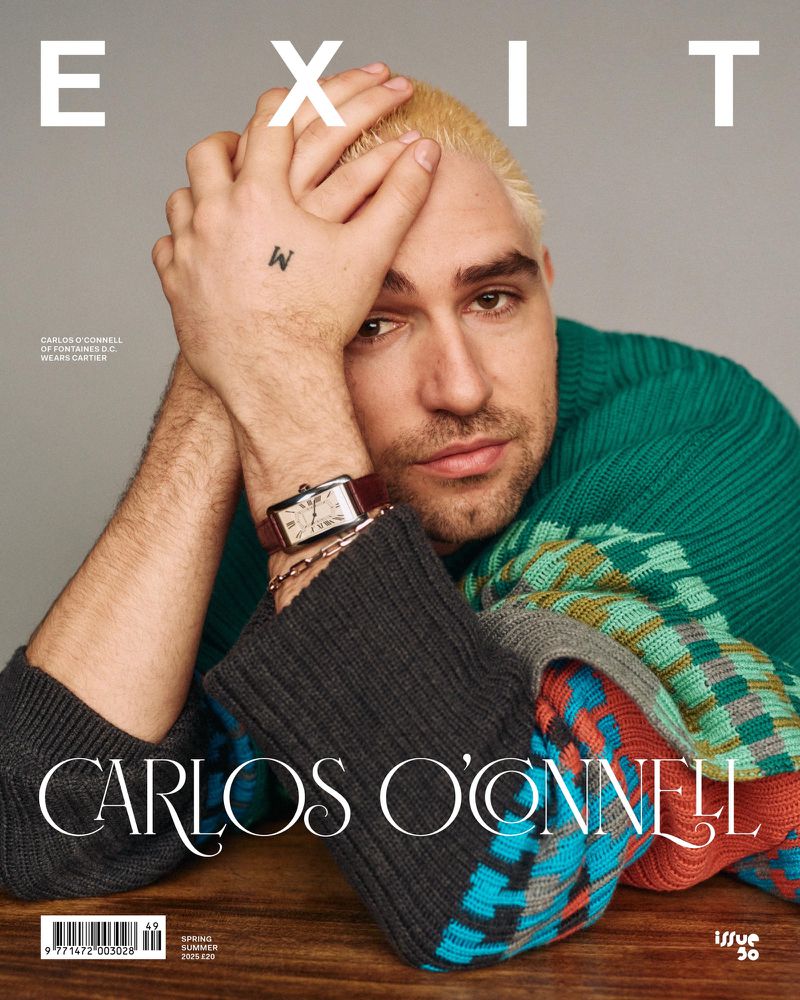 Magazine cover featuring Carlos O'Connell wearing a green patterned sweater, styled portrait, studio lighting, neutral background.