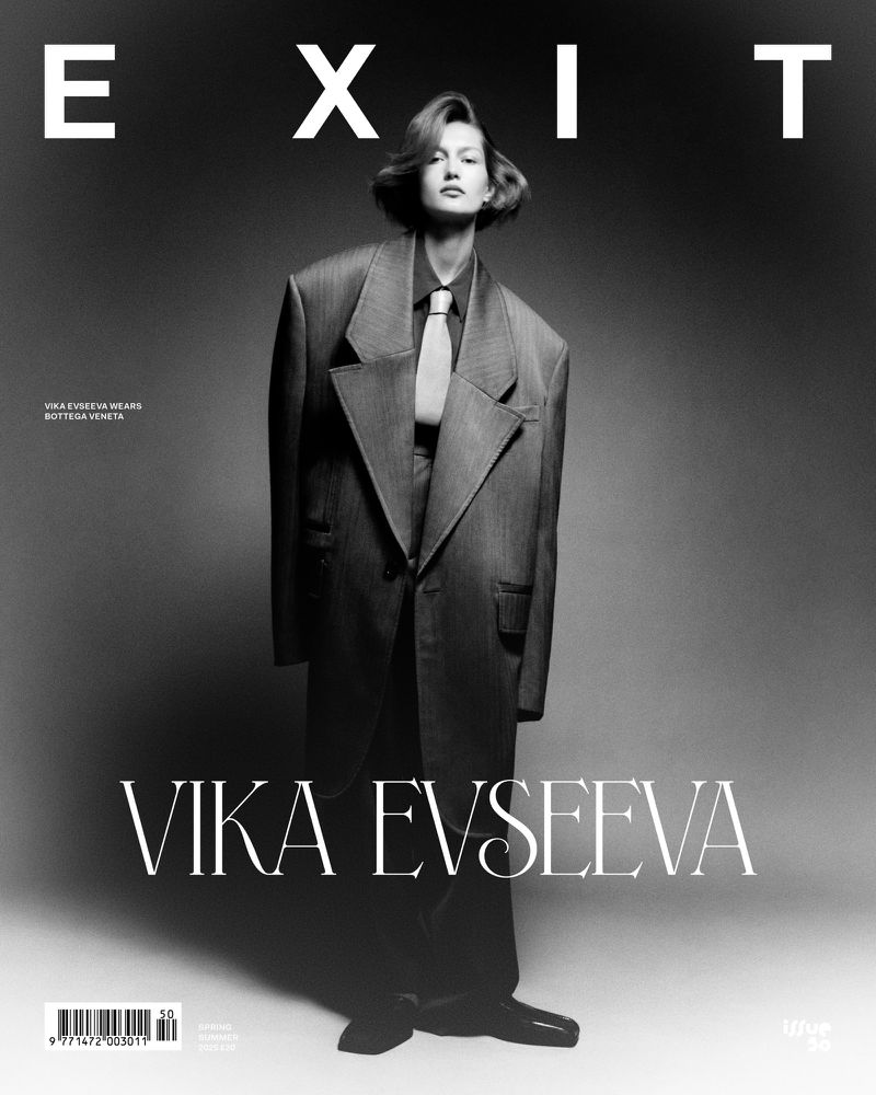 Monochrome portrait of Vika Evseeva on EXIT magazine cover, wearing an oversized suit with a tie, against a dark gray backdrop.