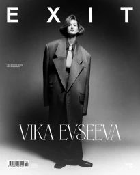 Black and white portrait of Vika Evseeva wearing an oversized suit jacket and tie against a seamless studio backdrop for Exit Magazine.