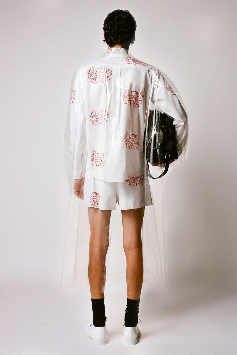 Back view of a slender adult male wearing a short white set with a red floral pattern, black socks, and white trainers indoors.