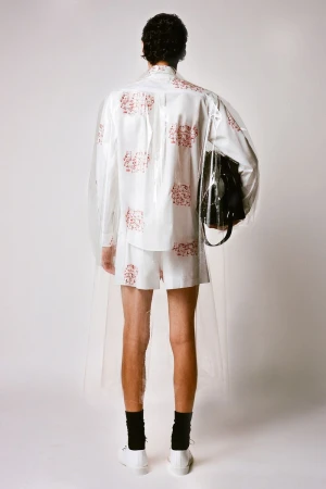 Back view of a slender adult male wearing a short white set with a red floral pattern, black socks, and white trainers indoors.