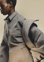 Model in grey button-down shirt and beige skirt wearing an oversized wool coat for Lacoste Entering Fall campaign.
