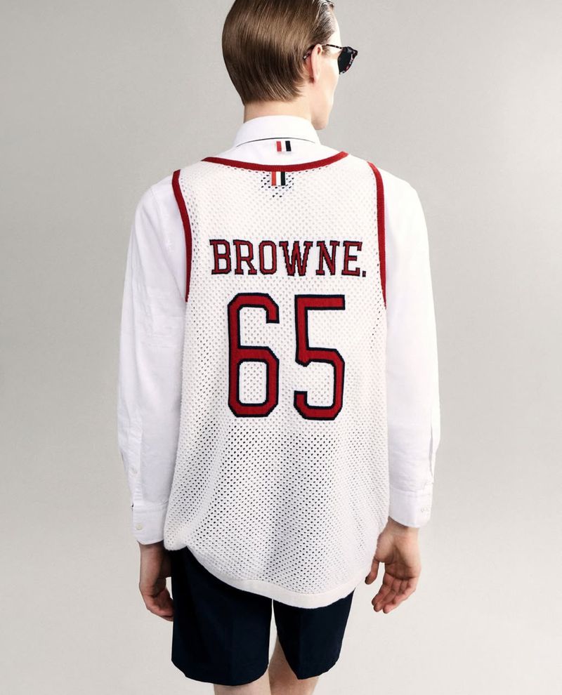 Back view of a slender adult wearing a white basketball jersey with 'BROWNE' and '65' in red, plus dark blue shorts.