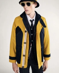 Model in yellow and black jacket wearing pinstripe suit, tie, sunglasses, and bucket hat against a neutral background