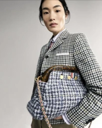 Model in houndstooth blazer holding tweed handbag against a white background for Thom Browne