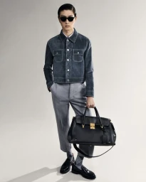 Male model in a grey suede jacket and trousers holding a black leather handbag against a plain background