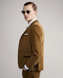 Profile view of a male model wearing round sunglasses and a camel corduroy blazer against a plain neutral background.