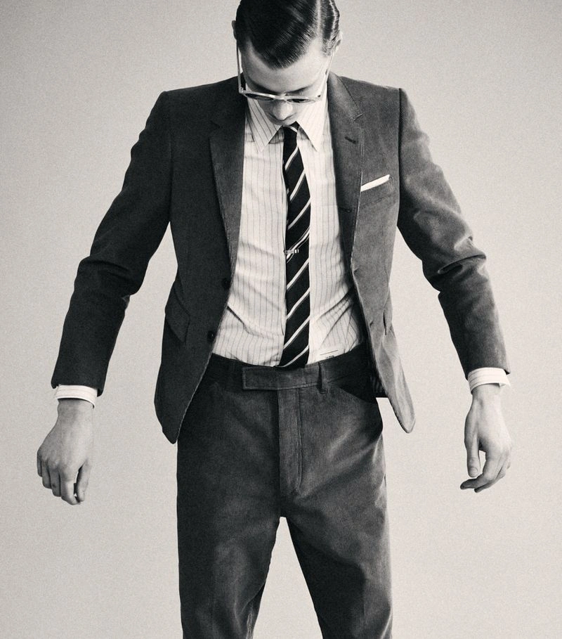 Man wearing a tailored grey suit jacket, striped shirt, and tie against a plain studio background.