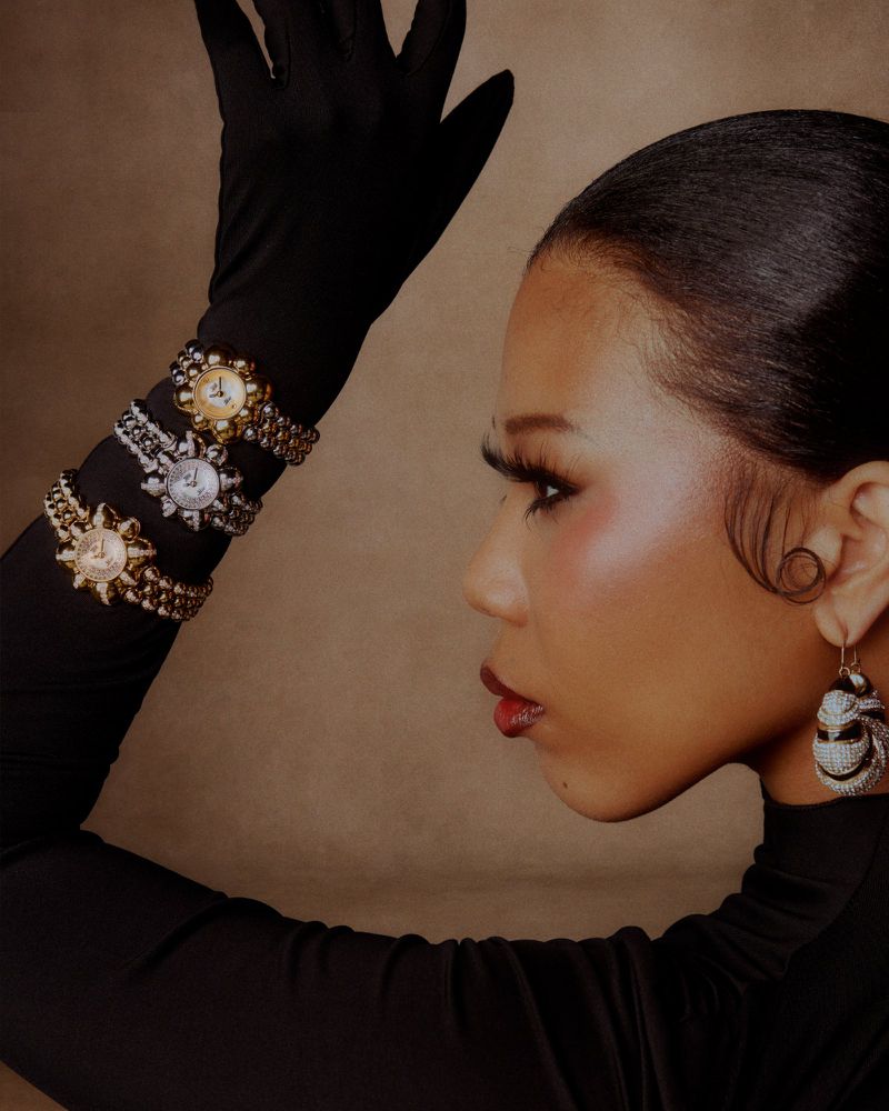 Profile of a woman wearing multiple luxury watches and an earring against a neutral background, showcasing jewelry and fashion details.