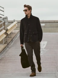 Man wearing dark jacket and trousers holding a black bag walking on an outdoor rooftop