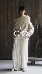 Model wearing cream draped attire standing against a vertical wood slat wall background.