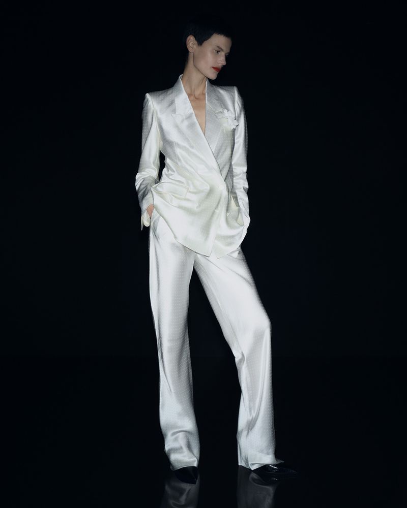 Elegant woman in a white suit posing against a black backdrop, showcasing sophisticated fashion and style in a studio environment.