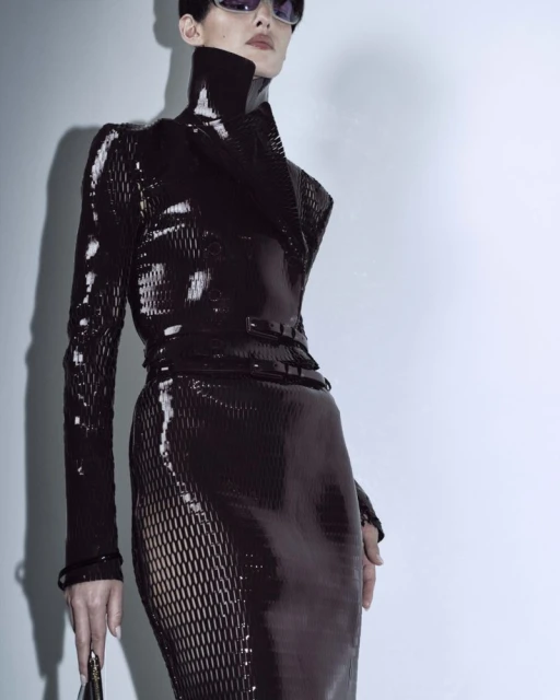 Fashion shot of a female model wearing a black shiny dress and sunglasses in a photo studio with a light background. 