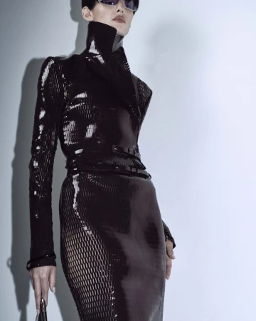 Fashion shot of a female model wearing a black shiny dress and sunglasses in a photo studio with a light background. 