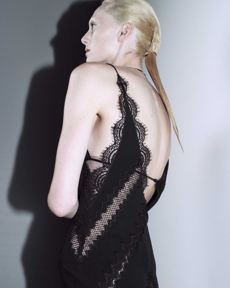 Model wearing a black lace dress against a grey studio backdrop with a sharp shadow cast