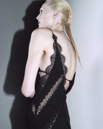 Model wearing a black lace dress against a grey studio backdrop with a sharp shadow cast