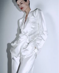 Model in a white satin blazer and matching trousers posing against a plain wall for Tom Ford S/S 2026.