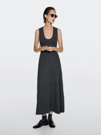 Adult woman poses wearing a gray dress, sunglasses, and black shoes in a studio with a bright white backdrop and even lighting.