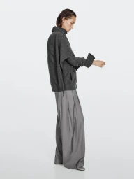 Model wearing a dark grey wool sweater and wide leg trousers against a plain white studio background.