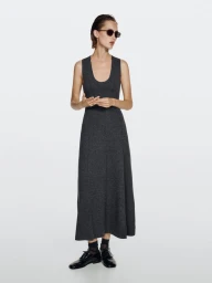 Model wearing dark sunglasses and a dark grey sleeveless maxi dress standing against a plain white studio background.