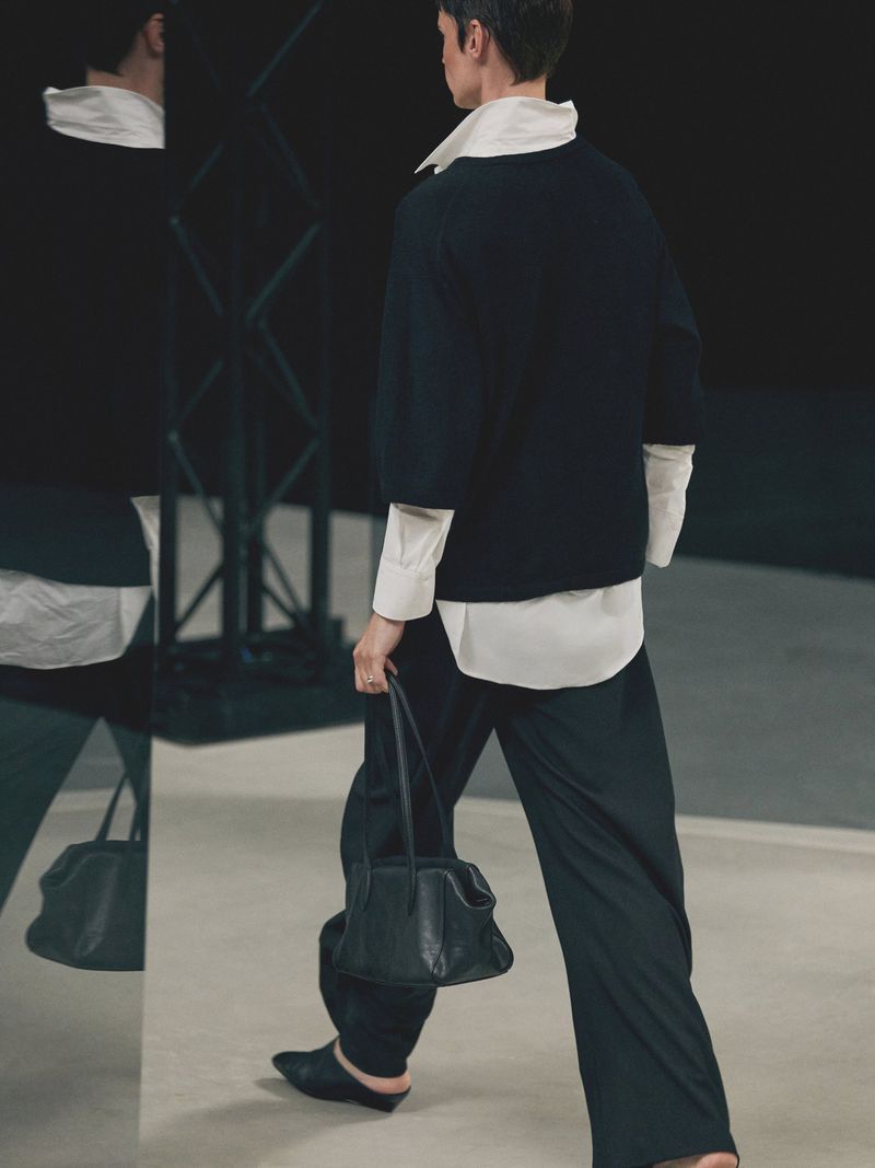 Woman in black sweater and pants walking with a black purse, shot from behind with a reflection and geometric metal art.