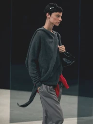 Model wearing a dark green hooded cashmere sweater and grey trousers holding a black handbag for Massimo Dutti