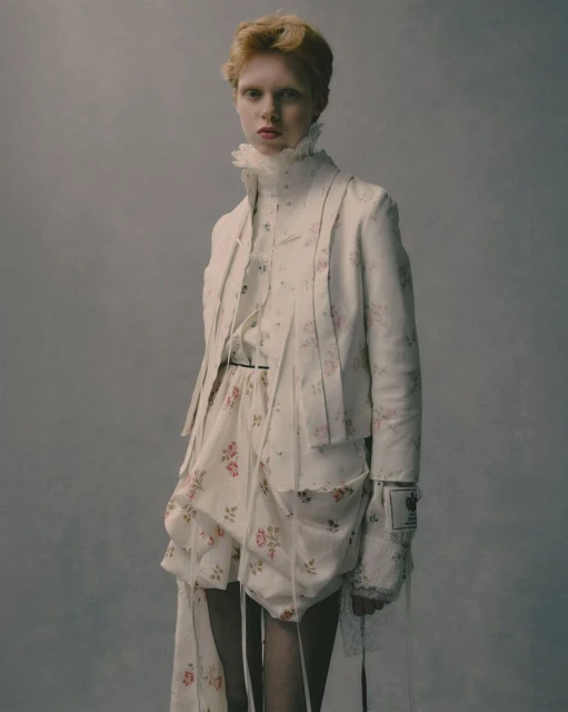 Young woman in a white floral jacket and shorts poses in a studio with neutral background. Fashion editorial portrait. 