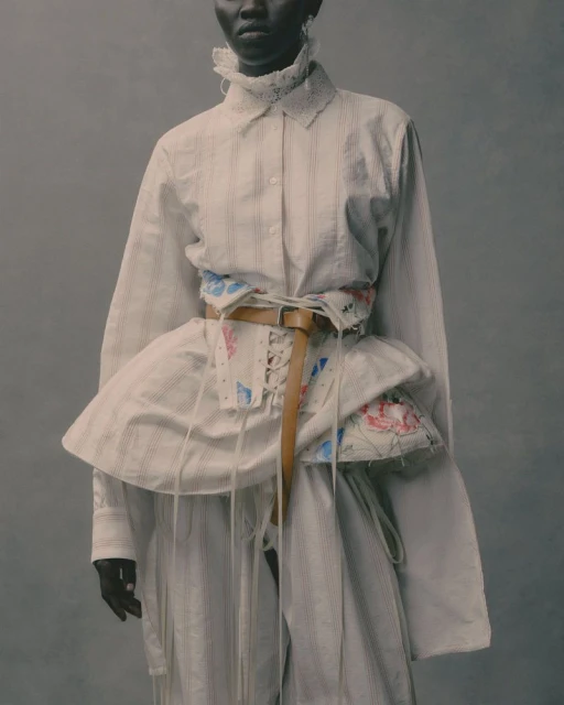 Dark-skinned model poses in a studio with a vintage-style white button-down, a floral corset, and matching striped pants, fashion-forward editorial.