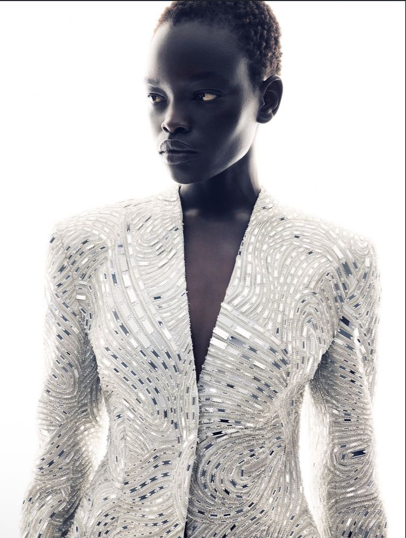 Model wearing a heavily embellished white jacket with silver reflective mosaic details against a bright white background.