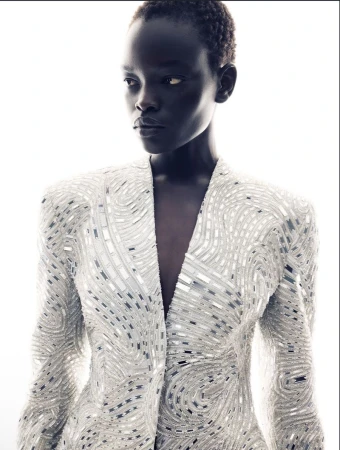 Model wearing a heavily embellished white jacket with silver reflective mosaic details against a bright white background.