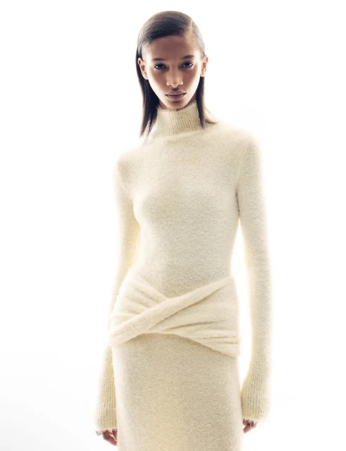 Elegant full-length portrait of a Black female model in a cream-colored knit dress against a bright white backdrop in a fashion studio.