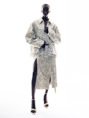 Model standing against a pure white background wearing a sparkling patterned metallic silver jacket and matching skirt.