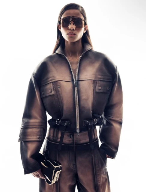 Fashionable adult female in studio lighting wearing a brown jumpsuit and sunglasses, holding a brown clutch.