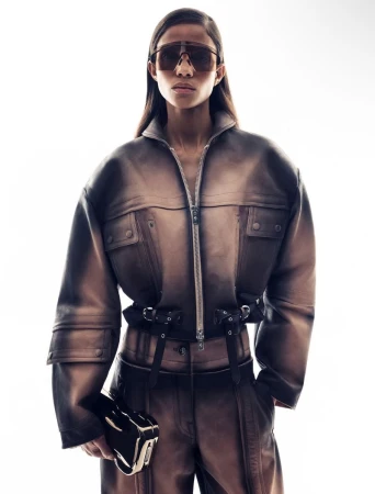 Fashionable adult female in studio lighting wearing a brown jumpsuit and sunglasses, holding a brown clutch.