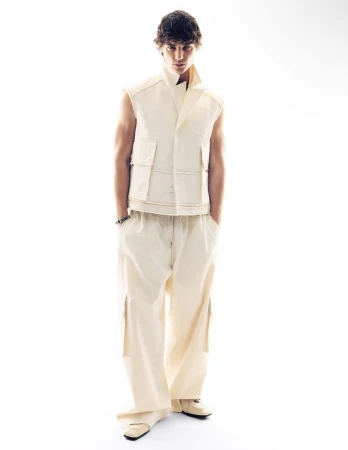 Male model in a cream vest and matching trousers standing against a plain white background