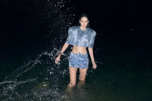 Model Vika Ihnatenko wearing a sparkling blue matching two piece set while standing in dark water with splashing droplets