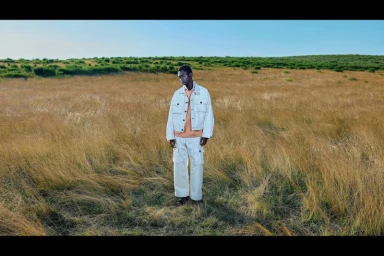 Model standing in a dry grassy meadow wearing a light-coloured jacket and matching trousers for N. Hoolywood