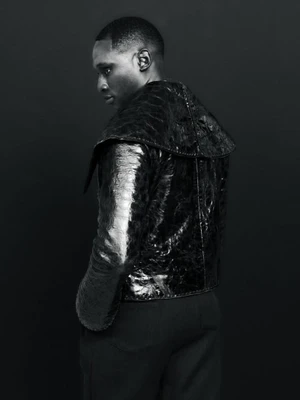 Black and white portrait of a man wearing a dark textured high-collar jacket against a dark background
