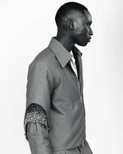 Black and white profile portrait of a male model wearing a collared jacket with embellished sleeve detail.